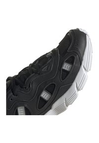 Schwarzer Sportschuh mit Mesh-Einsätzen und synthetischem Lederüberzug, ausgestattet mit einer dicken weißen Gummisohle und strukturierten Akzenten.