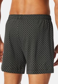 Shorts de bain noirs avec un motif géométrique blanc, taille élastique et coupe ample. Le matériau semble léger et texturé.