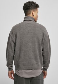 Suéter de cuello alto, de gran tamaño y color gris, confeccionado en material de punto suave, con puños y dobladillo acanalados, ajuste relajado y superficie texturizada.