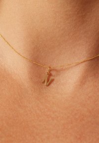 Collier en or avec une chaîne fine ornée d'un petit pendentif angulaire en forme de lettre "N". Le pendentif est plat et poli, reflétant la lumière.