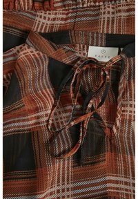 Blouse marron et noire à motifs, avec un col en forme de trou de serrure noué et une étiquette blanche visible indiquant "KAFFE."