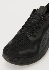 Baskets de course noires avec une tige en maille, des accents texturés et des détails réfléchissants. Présentent une semelle rembourrée et un système de laçage sécurisé.