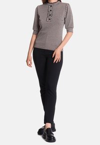 Figursydd rutmönstrad topp med rund halsringning, korta puffärmar och knappdetaljer, kombinerad med svarta smala byxor och kraftiga svarta skor.