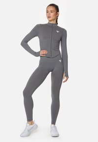 Gray athletic set featuring a zip-up long-sleeve top and high-waisted leggings. The material is smooth and stretchy, with subtle logo details.