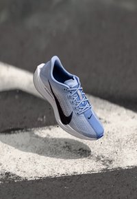 Baskets de course bleu clair avec une tige en maille, logo swoosh noir et semelle blanche. Présente une finition lisse avec des détails de ventilation.
