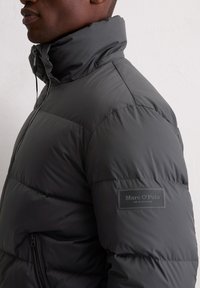 Grijze pufferjack met hoge kraag, soepele textuur, ritssluiting zakken en ‘Marc O'Polo’ label op de mouw, met een lichtgewicht ontwerp.