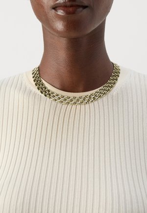 Collana di catena in oro con anelli intrecciati, indossata sopra un top a coste di colore chiaro. La vista ravvicinata mostra la superficie liscia e la finitura lucida.