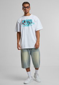White graphic t-shirt featuring blue and red text and star accents, paired with light wash denim shorts and white sneakers.