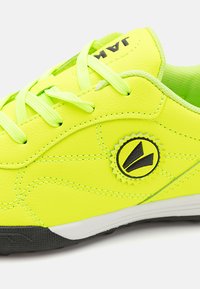 Sneaker giallo neon realizzato in pelle sintetica con lacci verde chiaro. Presenta una patch con logo nera e una suola in gomma nera testurizzata.