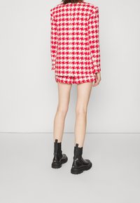 Blazer- och shortset i rutig design med röd och vit houndstooth-mönster, med en strukturerad design. Matchas med svarta ankelboots med tjock sula.