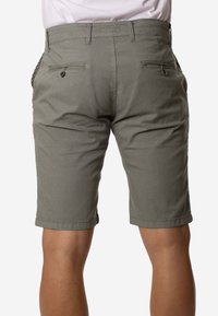 Hombre que lleva pantalones cortos grises hasta la rodilla con bolsillos traseros abotonados, mostrado de la cintura hacia abajo y por detrás.
