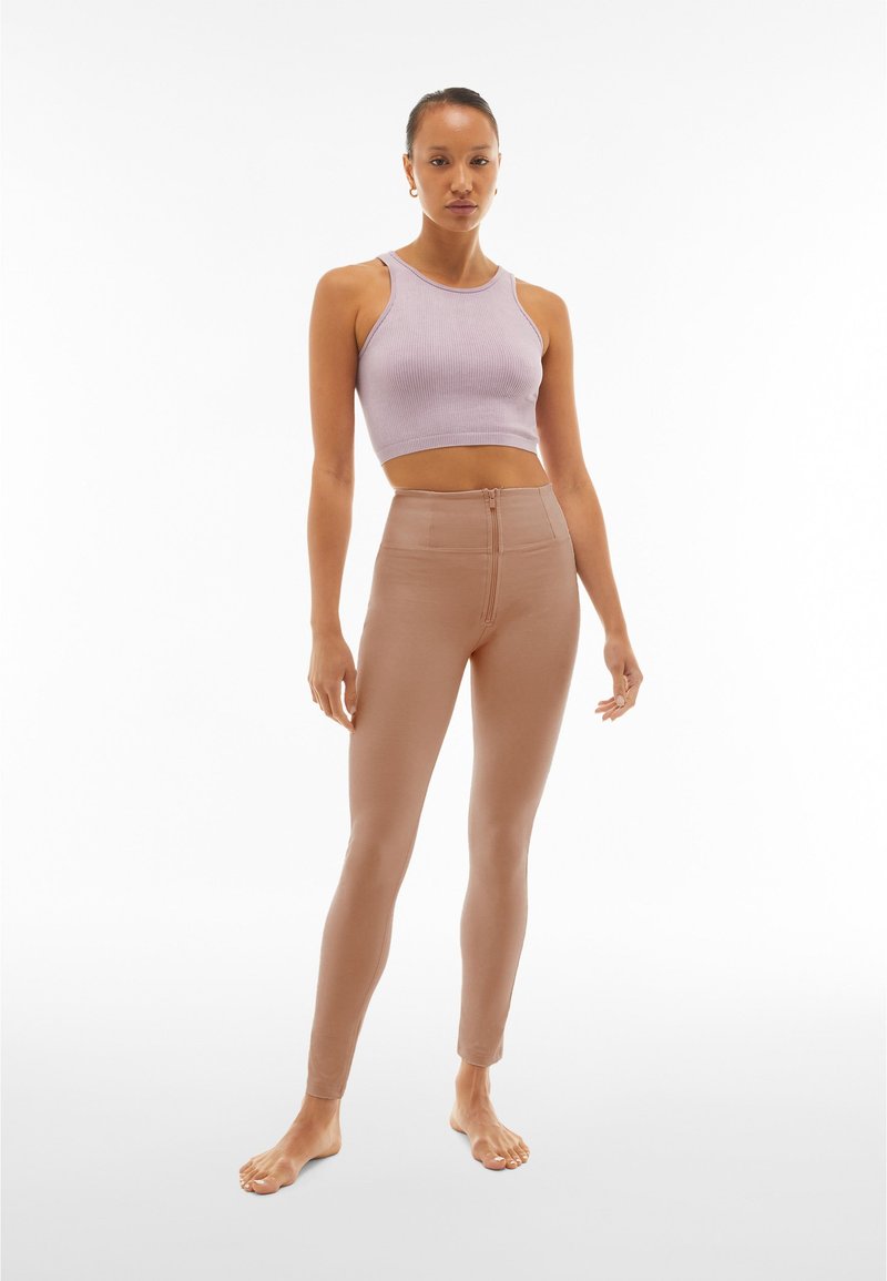 Crop top lilla chiaro a coste con scollo rotondo abbinato a leggings beige lisci a vita alta con cerniera frontale.