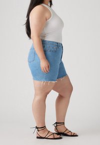 Shorts en denim léger bleu clair avec ourlet effiloché, associés à un débardeur blanc ajusté et des sandales noires à brides.