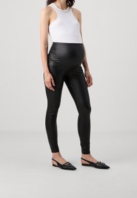 Černé legíny z umělé kůže s vysokým pasem, v kombinaci s bílým tílkem s texturovaným výstřihem. Celý outfit doplňují černé slingback byty.