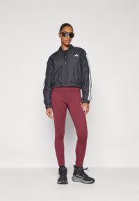 Črn bomberski jopič z belimi črtami, rdeče legice in črne športne čevlje. Gladek material z zadrgo na sprednji strani in elastičnimi manšetami.