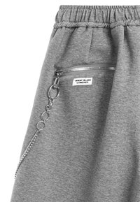 Pantalones de chándal gris con cintura elástica, un bolsillo con cierre y un largo detalle de cadena plateada adjunto al zipper del bolsillo.