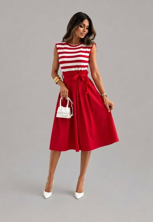 Femme portant un haut sans manches rayé rouge et blanc avec une jupe midi rouge, tenant un petit sac à main blanc et portant des talons blancs.