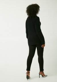 Schwarzer, gestrickter Langarmpullover mit geradem Schnitt, kombiniert mit schwarzen, enganliegenden Leggings und silbernen High-Heels. Einfaches Design, ohne Muster.
