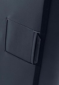 Borsa in tessuto nero con texture, caratterizzata da una tasca rettangolare con cuciture e un'etichetta sul lato che recita "INFORMAZIONI PROPRIETARIO BORSA".