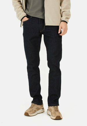 Dark blue denim jeans with a straight-leg cut, front pockets, paired with a beige zip-up fleece jacket and light tan sneakers.