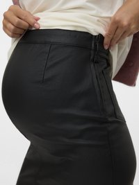 Schwarzer Rock aus Kunstleder mit figurbetontem Schnitt, glatt-texturiert und mit seitlichem Reißverschluss, kombiniert mit einem hellen Oberteil.