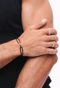 Brown leather bracelet with a gold link clasp, worn on a hand with two rings, one silver with stones and one gold with a geometric shape.
