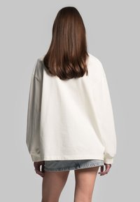 Oversized crèmekleurige sweatshirt met verlaagde schouders, geribbelde boorden en een gladde katoenen textuur, gecombineerd met lichtdenim shorts.