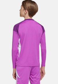 Maillot de sport à manches longues de couleur violette intense, avec des panneaux d'épaules violets foncés contrastants et des accents latéraux blancs. Tissu lisse et athlétique.