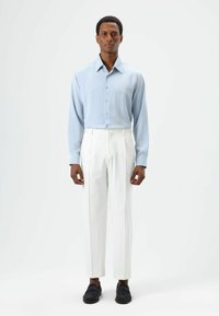 Light blue button-up shirt, tailored white trousers, and black shoes. The shirt has a smooth texture; trousers are pleated, structured fit.