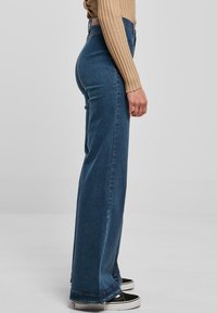 Hoge taille blauwe jeans met een rechte pasvorm, gemaakt van denim. Voorzien van een riemlus en subtiele stikseldetails aan de zoom. Gepaard met zwarte sneakers.