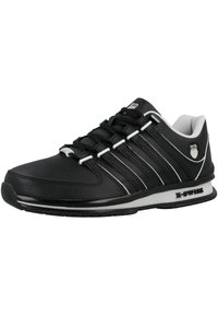 Scarpa atletica nera con tomaia in pelle sintetica, accenti bianchi a contrasto, punta arrotondata e interno imbottito bianco. Presenta lacci e marchi.
