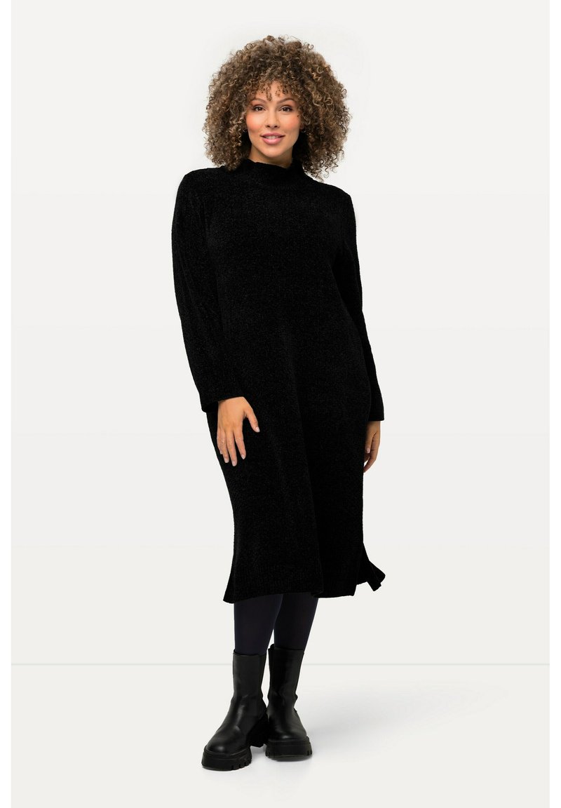 Abito nero a maniche lunghe con collo alto in un tessuto morbido e testurizzato. Presenta una vestibilità rilassata con spacchi laterali. Abbinato a stivali militari neri.