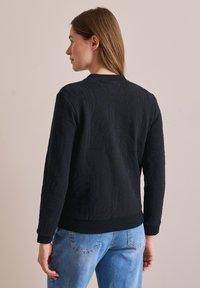 Suéter negro de punto con un patrón texturizado, con un dobladillo y puños acanalados, diseñado con un cuello redondo y un ajuste ceñido.