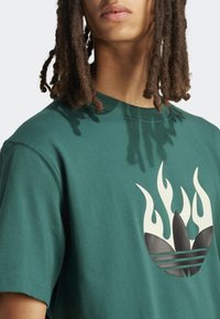 T-shirt in cotone verde con un grande motivo a fiamma in crema e nero, con scollo rotondo e maniche corte.