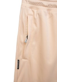 Jasnopomarańczowe spodnie sportowe z teksturowanym wykończeniem, z elastycznym paskiem w talii, boczną kieszenią na zamek oraz metką z logo po lewej stronie.