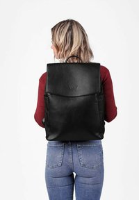 Černý kožený batoh se strukturovaným designem, horním klopovým víkem a vyraženým logem. Obsahuje dvě boční kapsy a horní rukojeť na nošení.