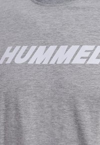 Camiseta de algodón gris con un prominente logo en blanco "HUMMEL" en el pecho, cuello redondo simple y textura suave y lisa.