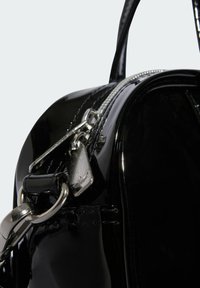 Sac à main en cuir verni noir avec une finition glossy, doté d'une fermeture éclair et de quincailleries en argent, y compris une petite étiquette logo et des poignées robustes.