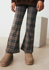 Pantaloni a zampa d'elefante in plaid blu scuro, giallo e rosso. Realizzati in tessuto morbido. Indossati con stivali alla caviglia in suede marrone.