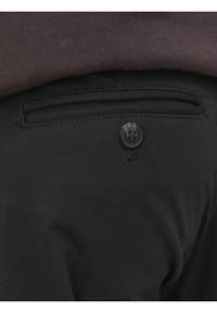 Pantalones de tela negra con un bolsillo trasero con cierre de botón, textura suave y un ligero brillo en el material.