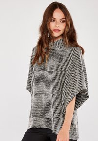 Poncho texturizado en blanco y negro con un cuello alto y un ajuste holgado, que presenta mangas amplias y un patrón a rayas.