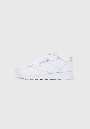 Biały klasyczny skórzany sneaker Reebok z sznurowadłami i widocznym logo marki na boku i pięcie, pokazany z profilu na jednolitym tle.