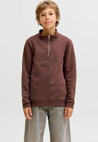 Sweatshirt zippé marron avec un col haut, logo "ORIGINALS" brodé et poignets côtelés. Porté avec un pantalon large gris clair.