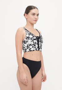 Top corto floreale in bianco e nero con scollatura lacciata e spalline regolabili, abbinato a slip bikini neri a vita alta. Texture liscia.