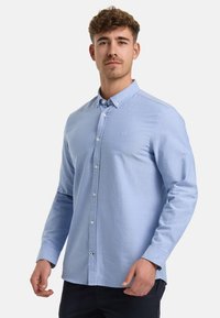 Camicia azzurra chiara a maniche lunghe con colletto button-down e un piccolo logo sul petto. Tessuto morbido con una leggera texture.