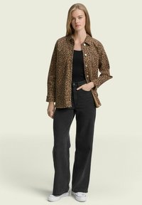 Leopardprint shirt jacket in bruine tinten, met knoopsluiting aan de voorkant, gecombineerd met zwarte high-waisted jeans en witte sneakers. Zachte textuur.