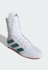 Stivale sportivo bianco con tomaia in mesh testurizzato, caratterizzato da tre strisce diagonali verdi e una suola in gomma con finitura liscia.