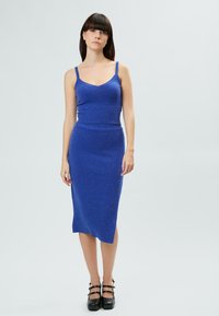 Blaues Strickkleid mit Spaghettiträgern, geripptem Oberteil und geradem Rock. Verfügt über dezente Glitzerpartikel, eine Länge bis zur Mitte der Wade und einen asymmetrischen Saum.