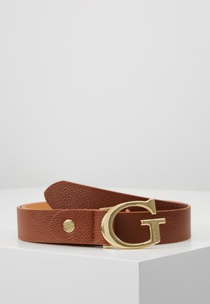 Ceinture en cuir marron texturé avec une grande boucle dorée en forme de « G » reposant enroulée sur une surface blanche.