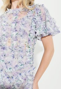 Durchscheinendes Blumen Kleid in Flieder und Grün mit gestuften Rüschendetails an den Ärmeln und dem Saum, das die weiche Textur und die zarten Muster betont.